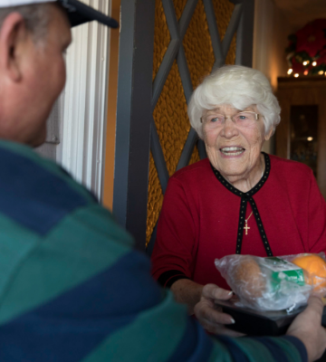 Volunteer handing meal tray to smiling client at door.