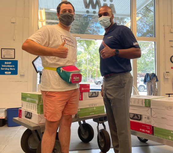 Jason Peace and young, male volunteer pose with their thumbs up in front of a cart of donated box fans.