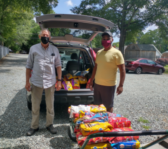 Two volunteers stand outside of a trunk full of pet food.