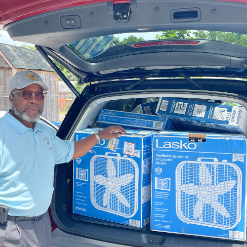 Man holding box fans in the back of his car trunk full of box fans.