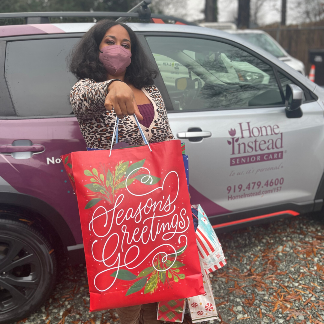 Volunteer Associate holds holiday gift out in front of a car.