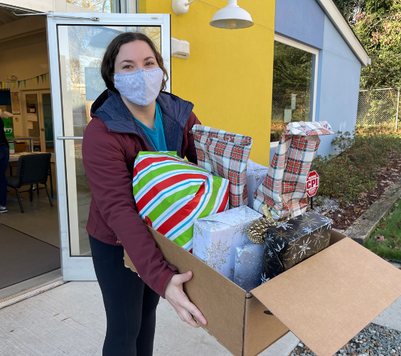 Volunteer holding a box full of wrapped holiday gifts.