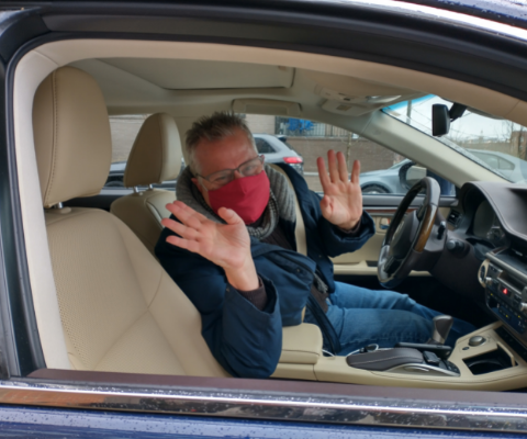 Delivery driver smiling and waving at driver's seat of his vehicle.