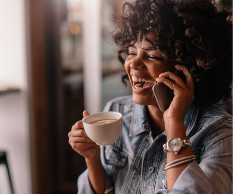 Young lady smiling and laughing while talking on the phone with a coffee mug.