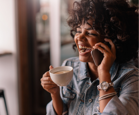 Young lady laughing on the phone will holding a coffee mug.