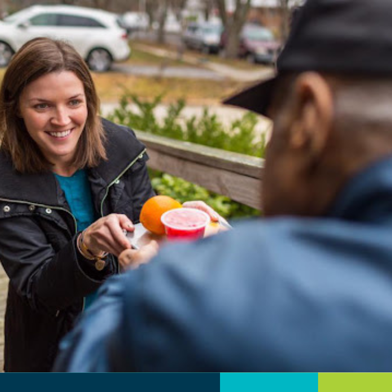 Young lady handing meal tray to client