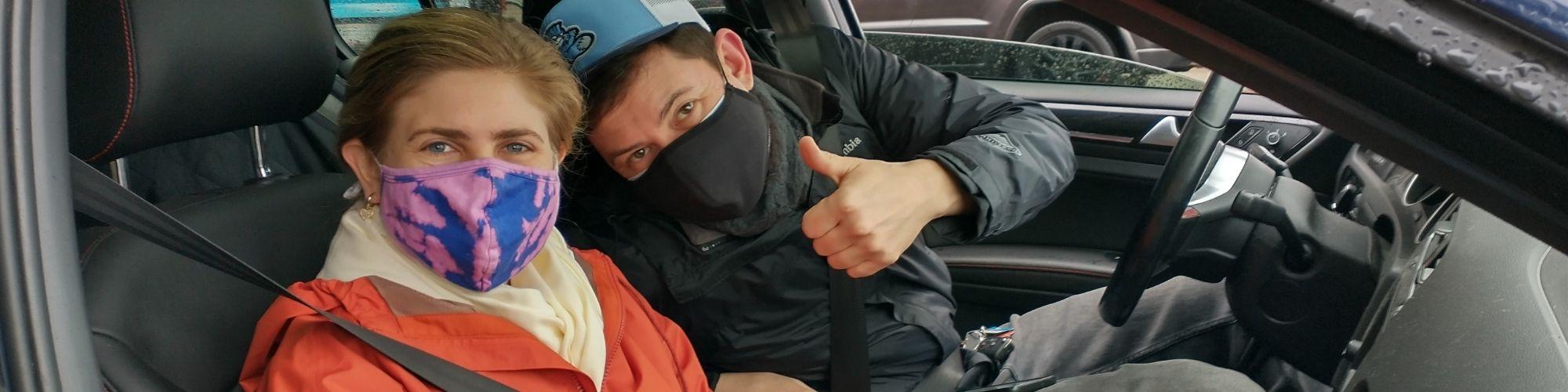 Two volunteer drivers in the front seat smiling under their facemasks, with the male volunteer showing thumbs up.