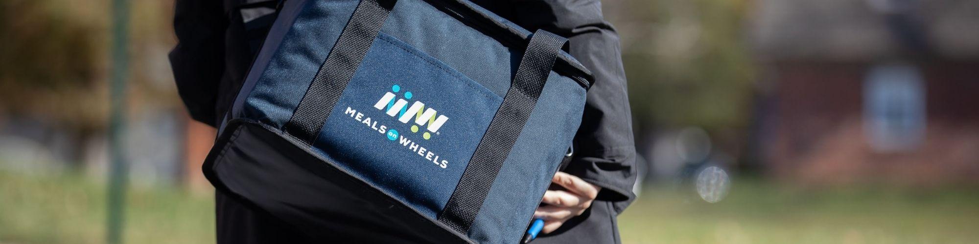 Volunteer holding meals on wheels meal cooler bag.