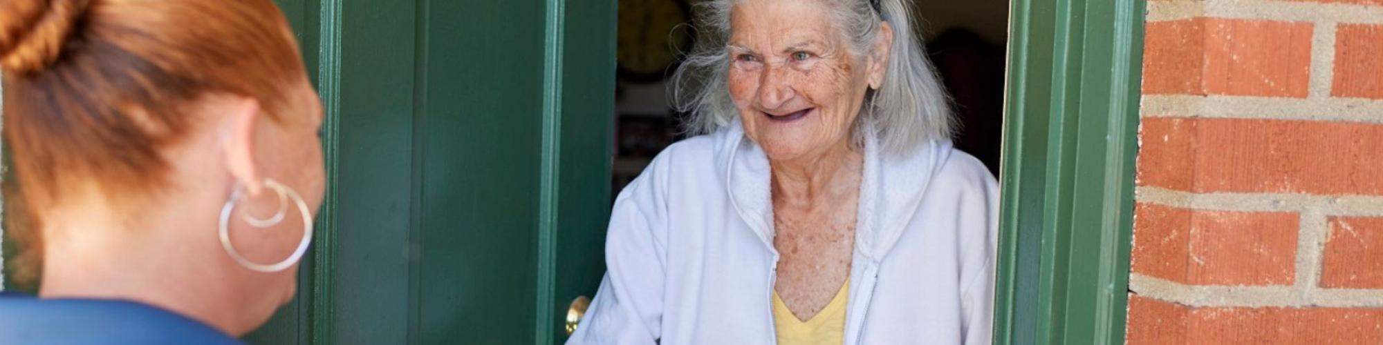 Volunteer handing meal to smiling client at green front door.