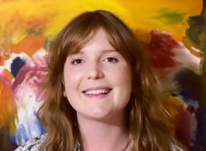 Libby Towell professional headshot smiling in front of a multicolor, painting-like background.